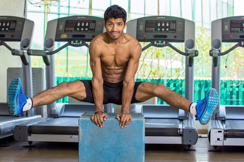 Shirtless muscular man performing calisthenics in an indoor gym in Chandigarh, India.